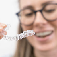 smiling woman using clear plastic removable braces aligner or whitening tray. dental orthodontic care.