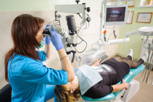 Woman dentist working with microscope at modern stomatological clinic. Teeth care and tooth health. Dentist checking patient teeth looking through the microscope. Stomatology equipment